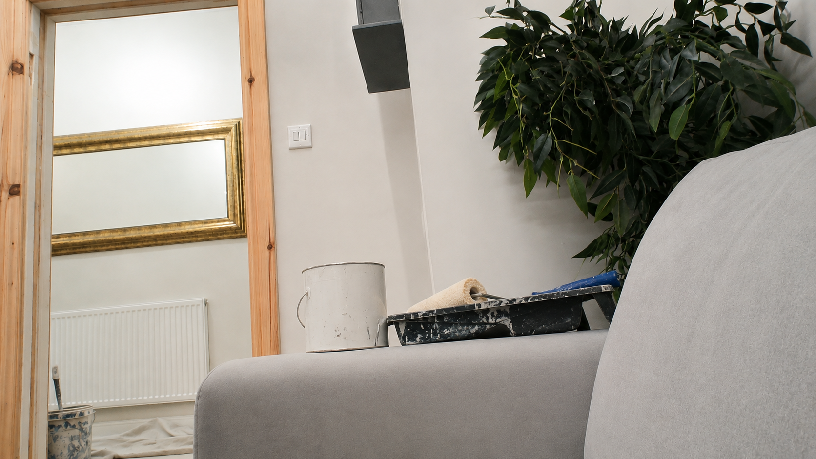 A room being decorated, with paint tins, a roller tray and a mirror