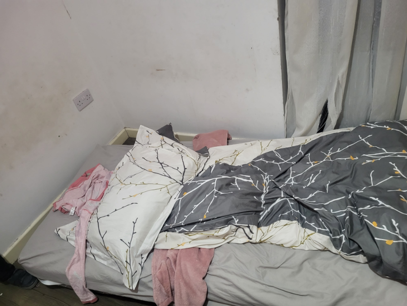 A bed made up with a grey and white patterned duvet and warm pink layers